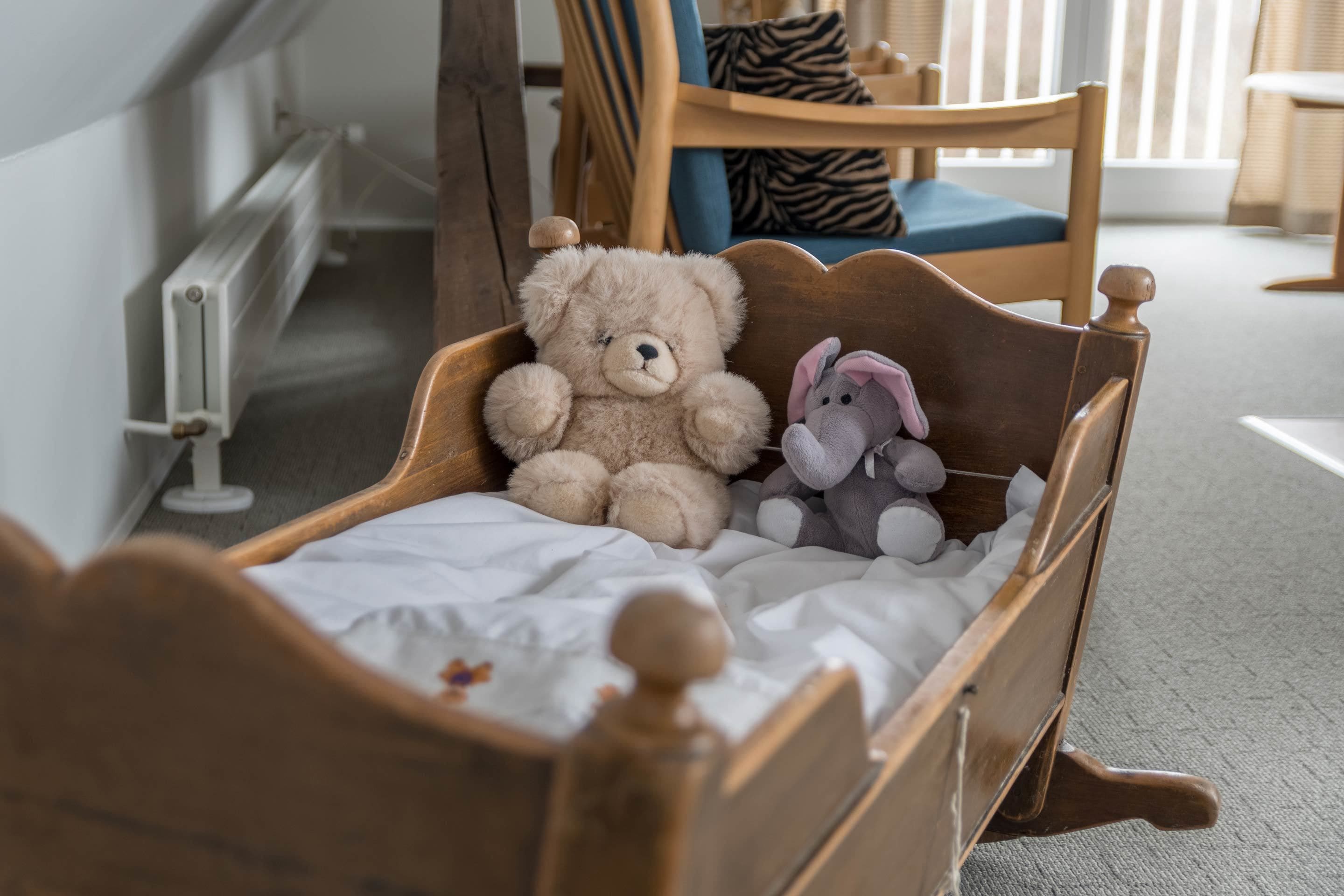 A wooden bed with a white sheet, a teddy bear, and a stuffed elephant.