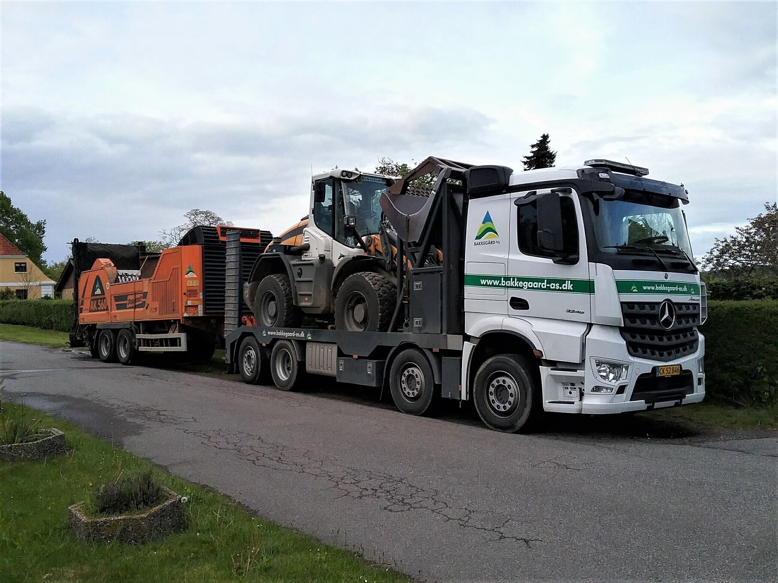 Um caminhão branco com um semirreboque laranja grande transportando um maquinário volumoso.