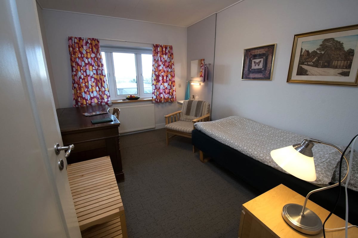 A compact room with a bed, a desk, a chair, and a lamp.