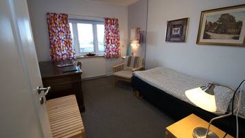A compact room with a bed, a desk, a chair, and a lamp.