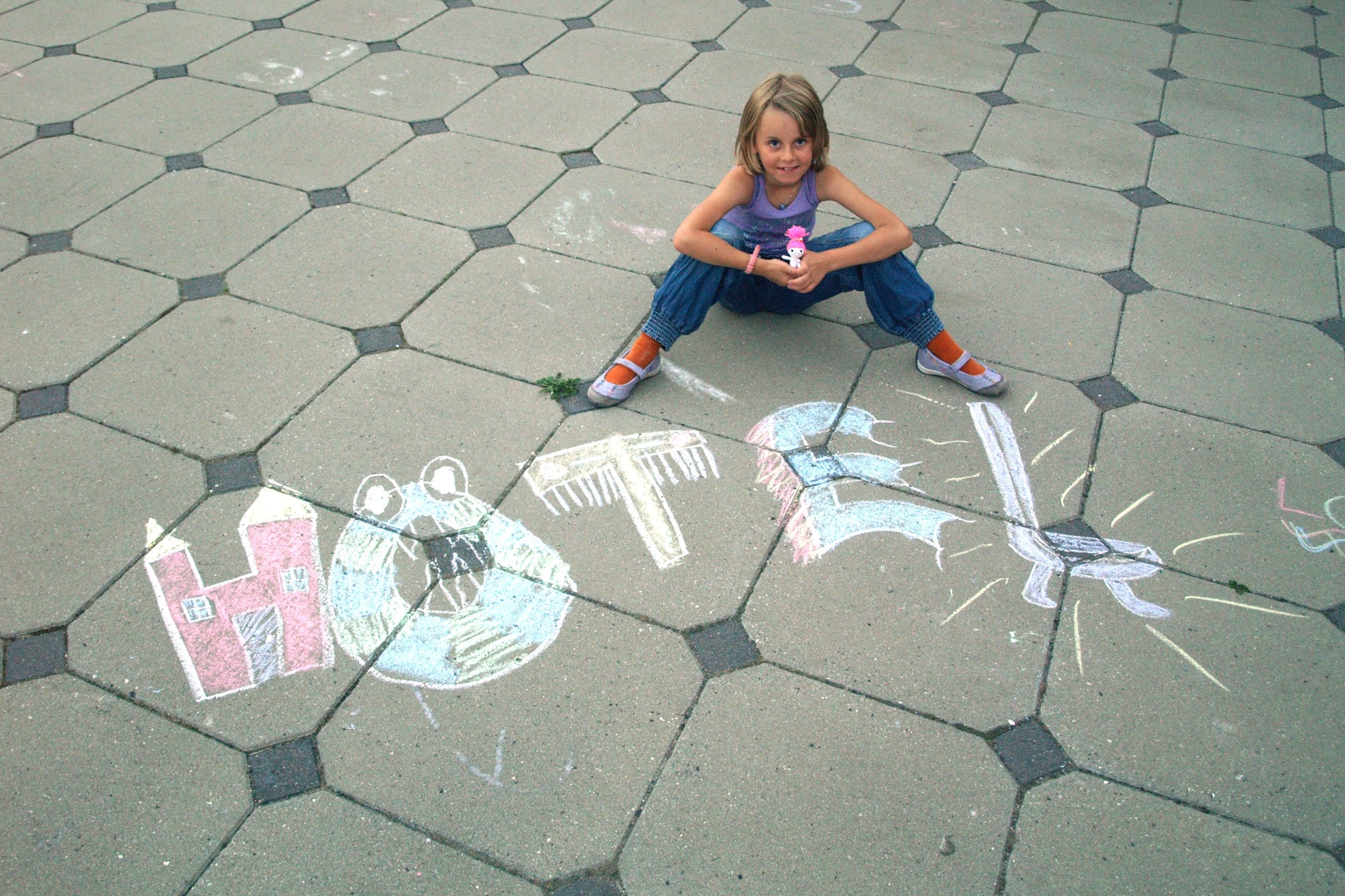 A child sitting on a hexagonal tile floor with chalk drawings of a house and a sword.
