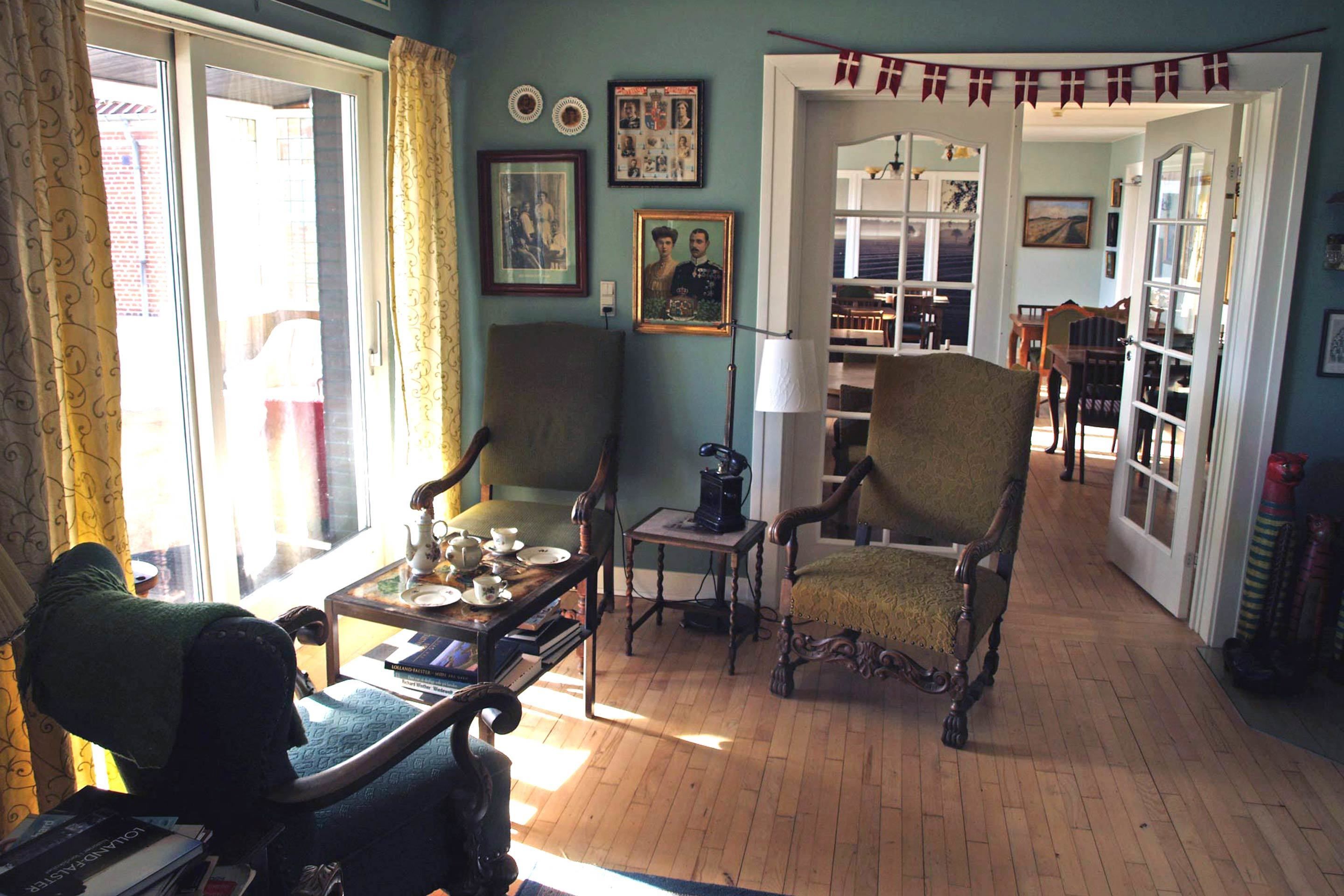 A traditional room with wooden flooring, two armchairs, a table with a lamp, and a bookshelf.