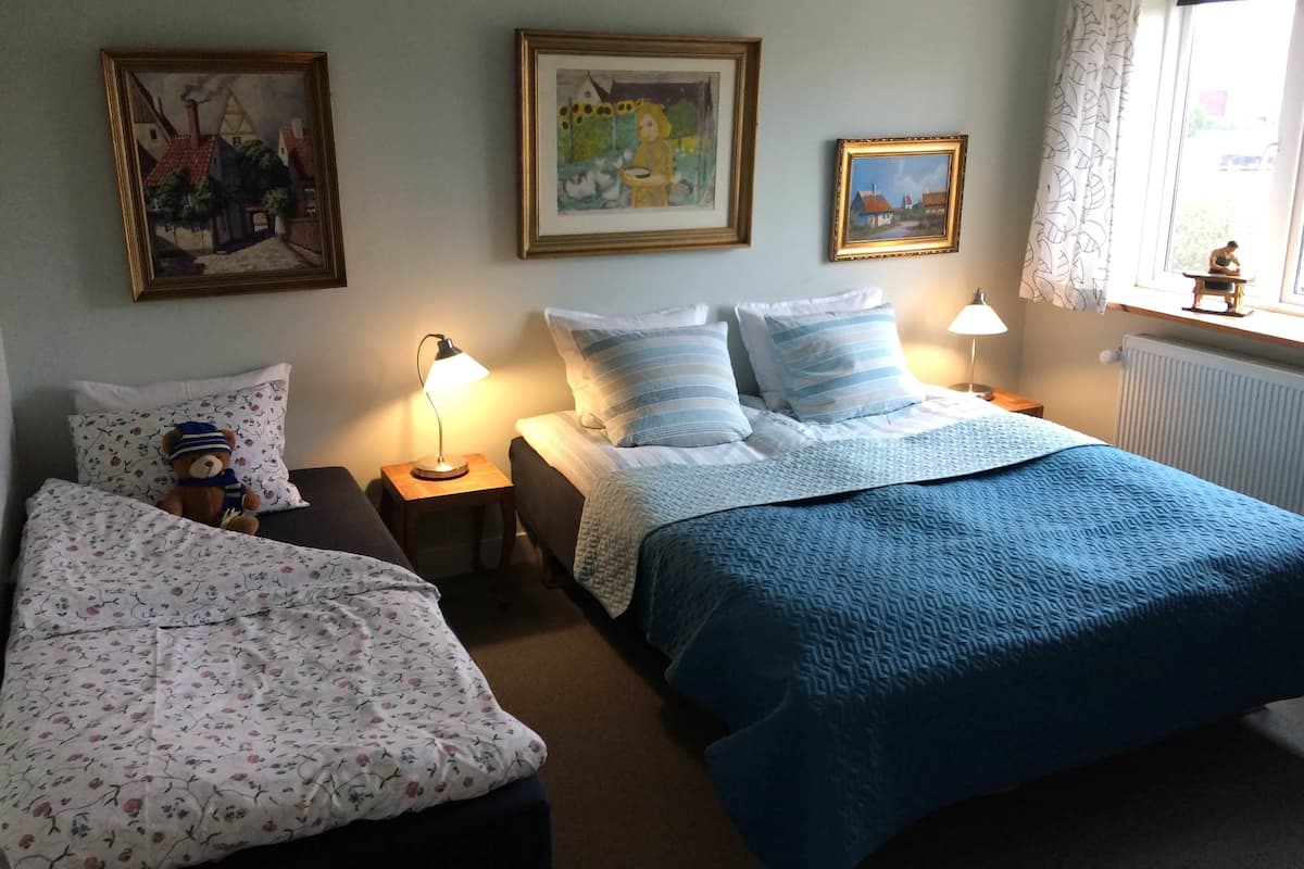 A room with two beds, a nightstand with a lamp, and framed artwork on the walls.