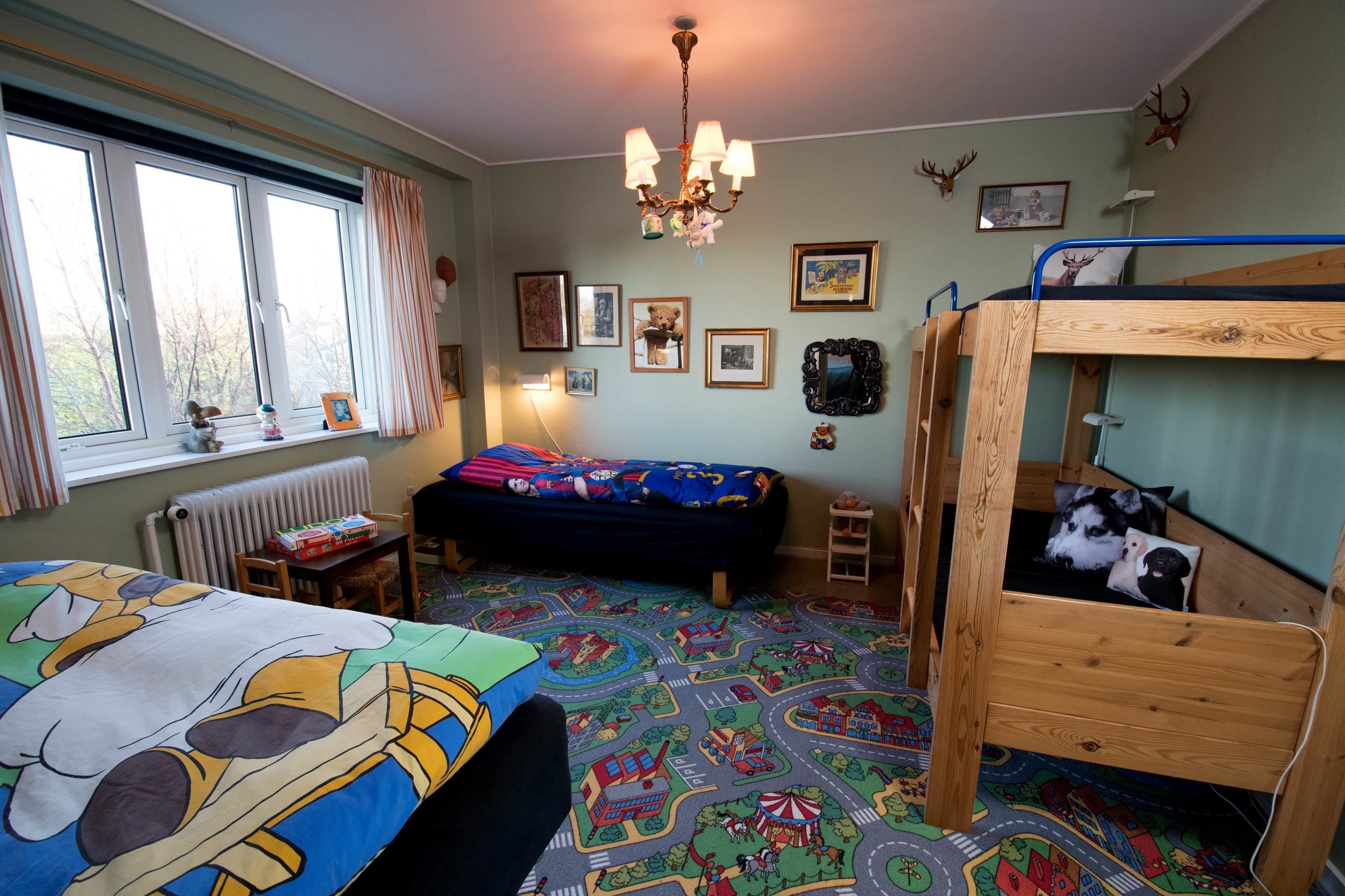 Een kinderkamer met stapelbedden, een raam met gordijnen, een radiator en diverse wanddecoraties.