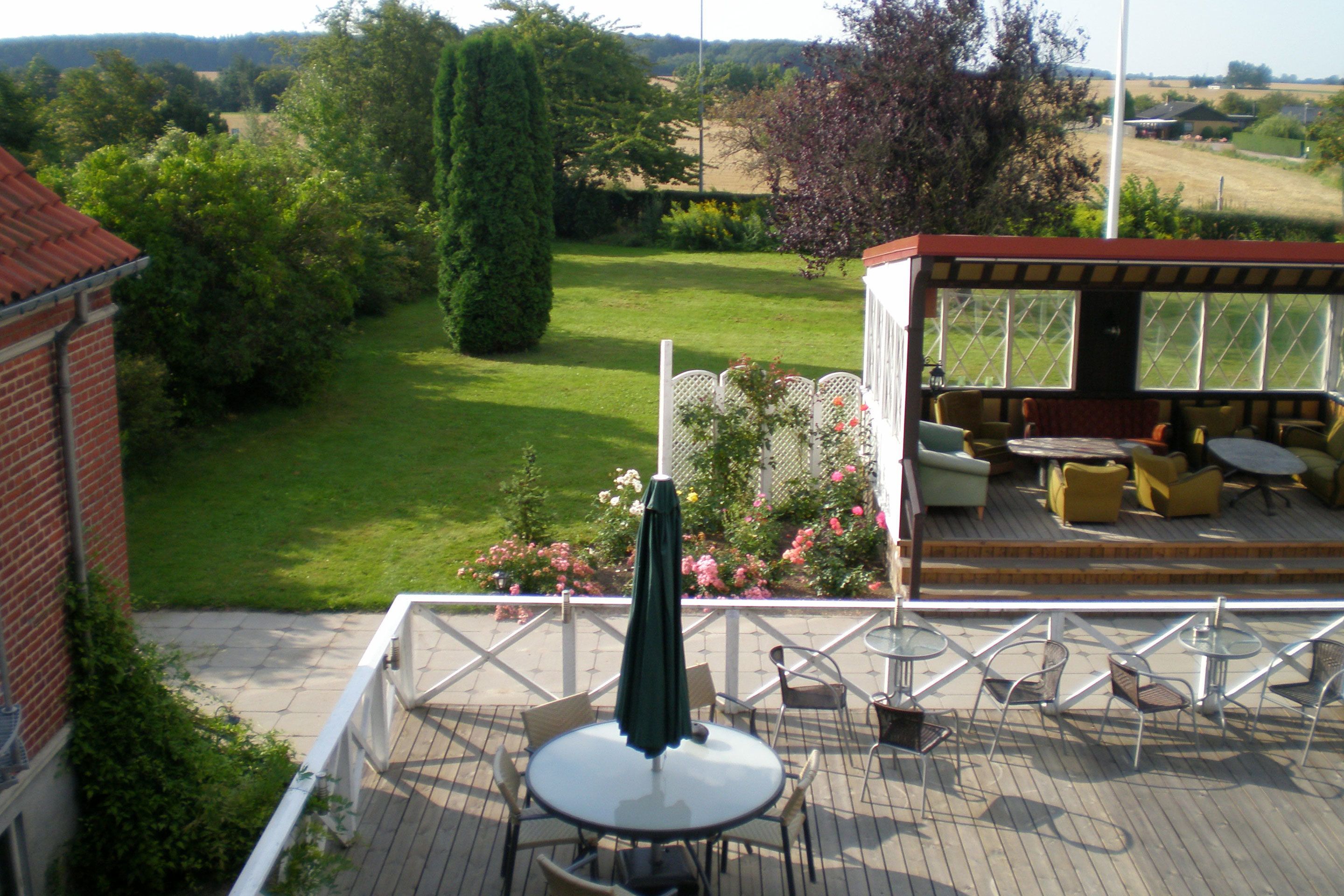 A patio with a table and chairs, a covered seating area with sofas and a table, and a view of a grassy yard with trees and a building in the background.