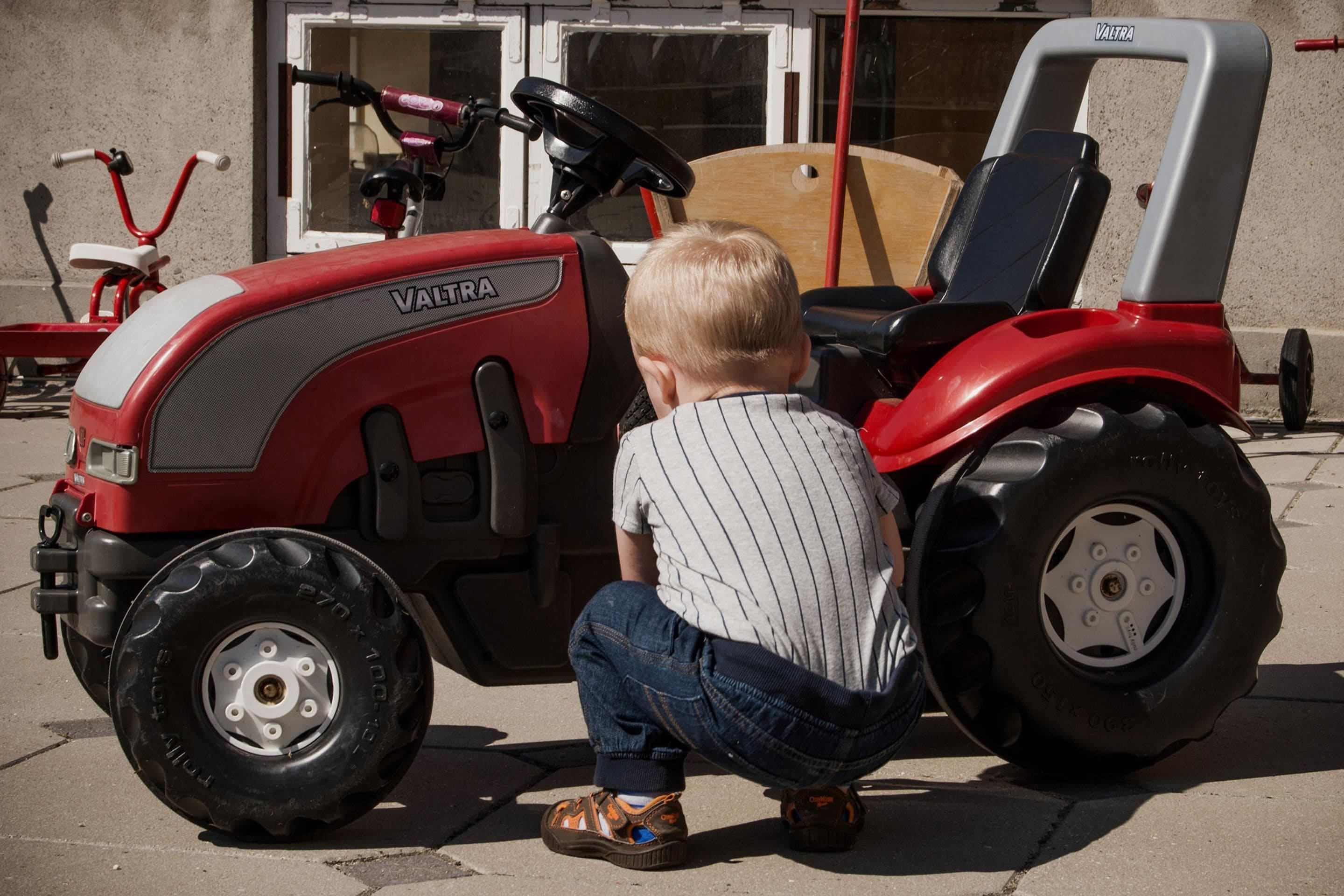 Un niño agachado junto a un tractor rojo.