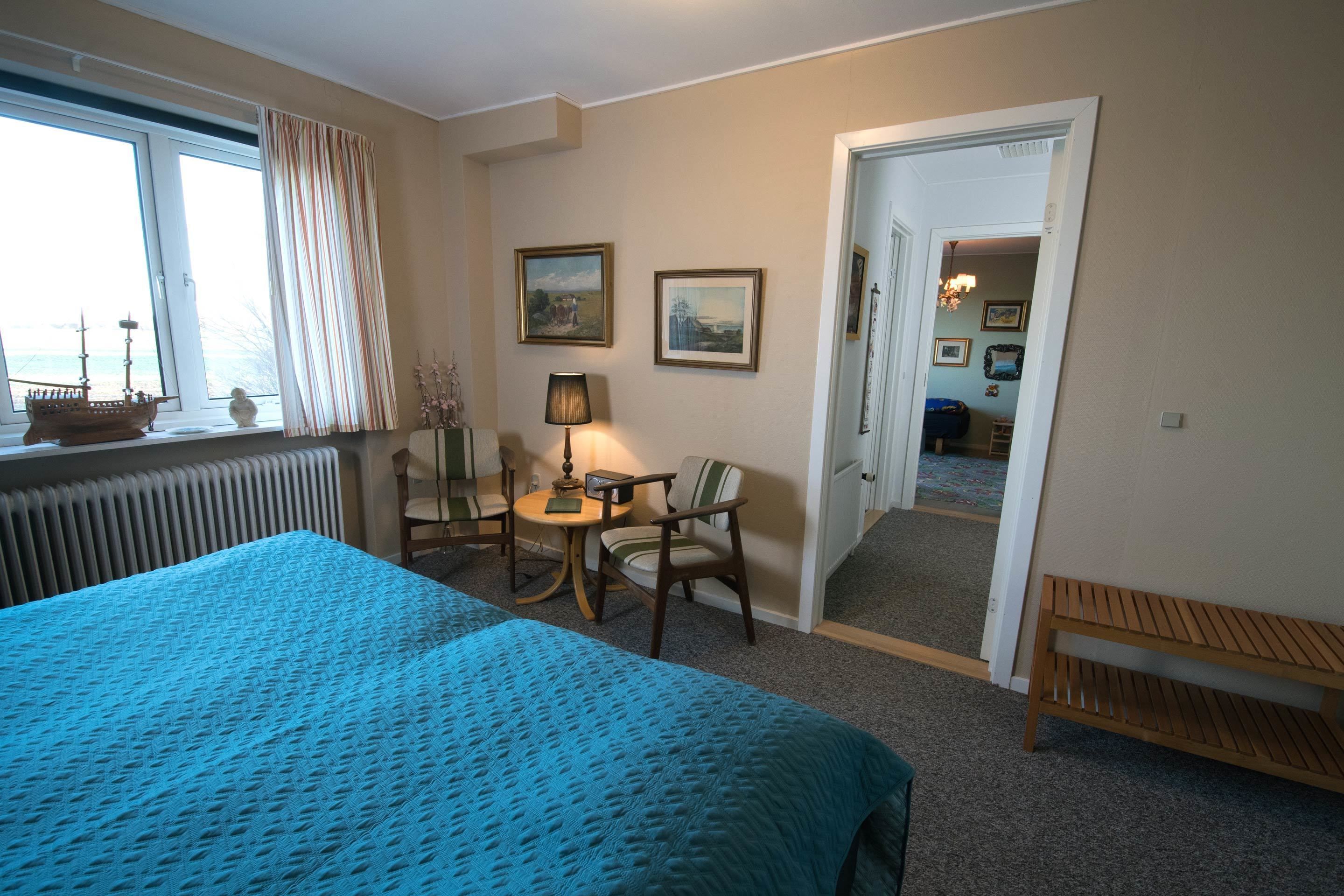 Et hotelværelse med en stor seng, et lille bord med stole, en lampe og to billeder i rammer på væggen.