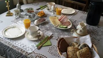 A breakfast table set with plates, cups, a teapot, a thermos, and a basket of bread.