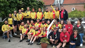 A group of people in yellow and red sports attire posing in front of a brick building with a red-tiled roof.