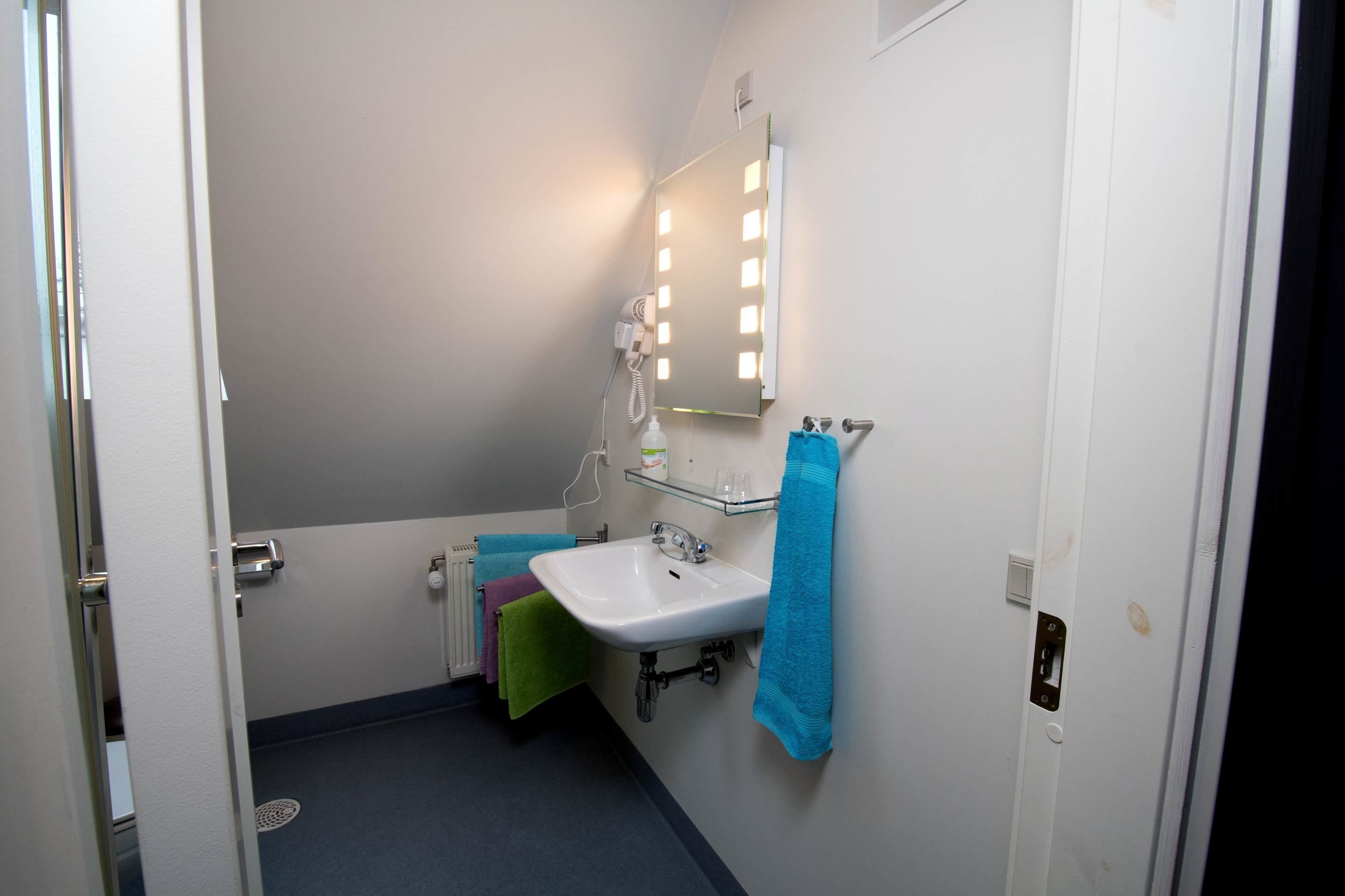 A bathroom with a white sink, a mirror with lights, and towels hanging on the wall.