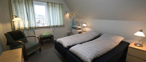 Un dormitorio con cama, una silla, un escritorio y una ventana con cortinas.
