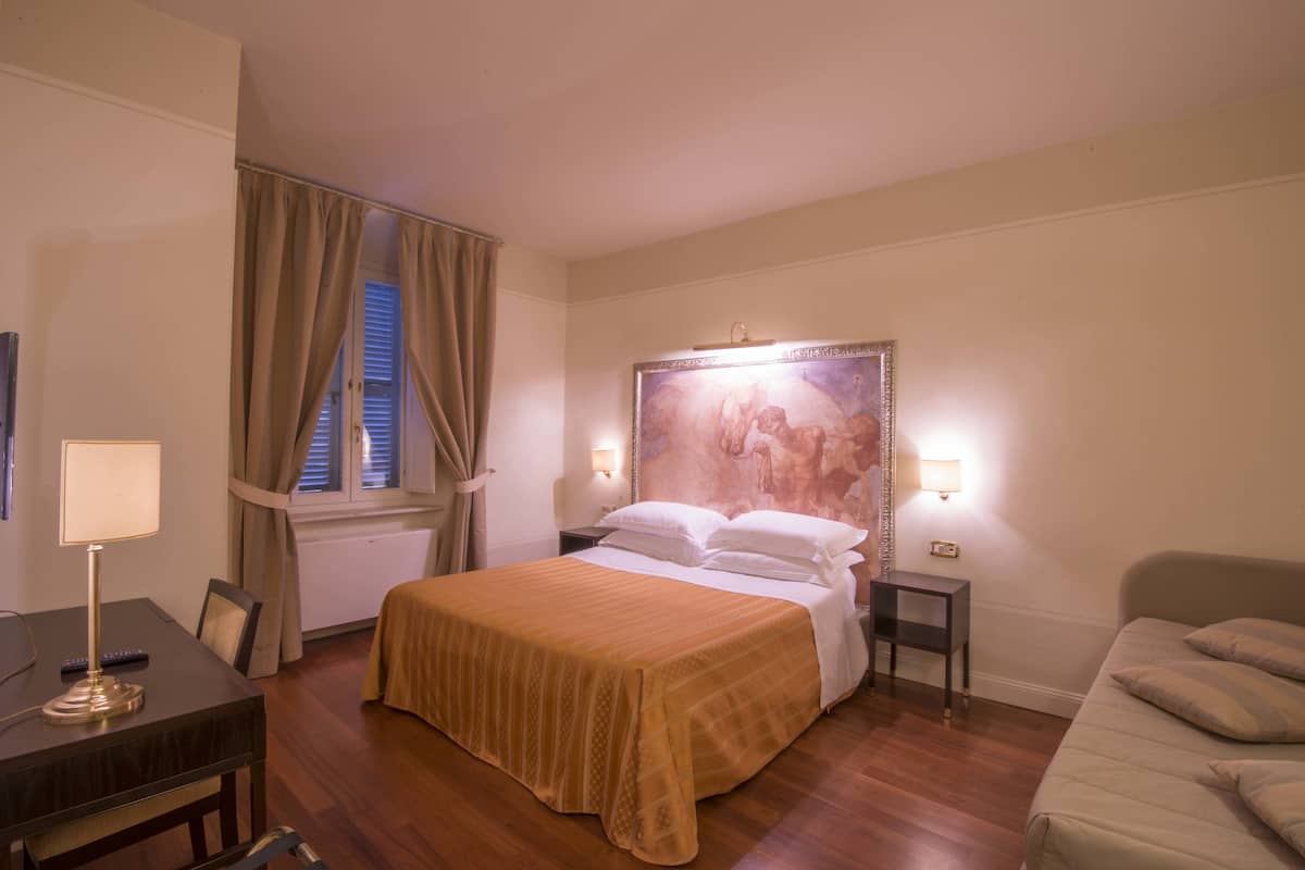 A hotel room with a bed, bedside tables, a desk, and a window with curtains.