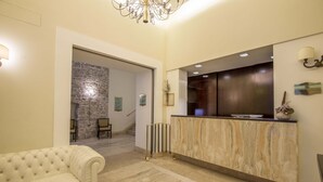 A reception area with a marble reception desk, a cushioned sofa, and a stone wall in the background. - Albergo Sant'Emidio (Ascoli Piceno)