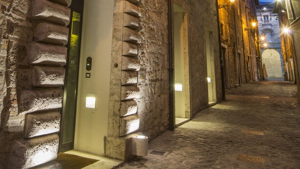 A narrow cobblestone street with historic buildings, a sign for Albergo S. Emidio, and a stone archway. - Albergo Sant'Emidio (Ascoli Piceno)