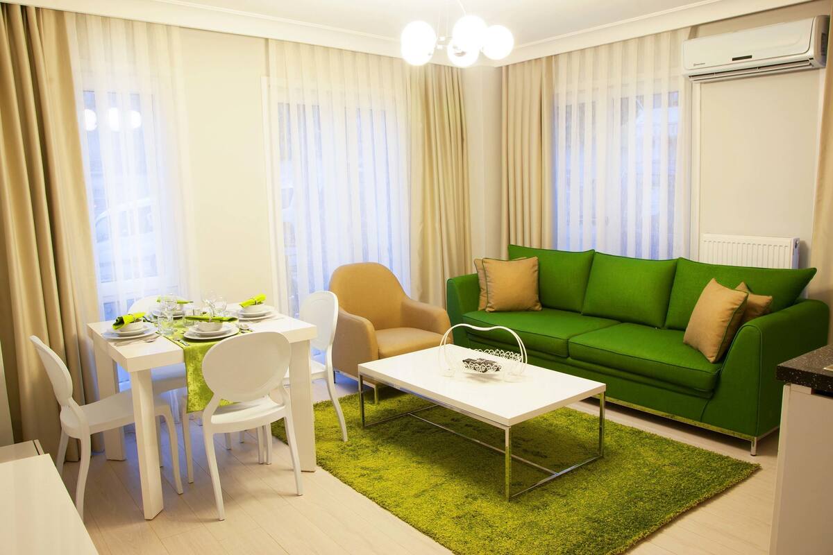 Un salon moderne avec un canapé vert, une table à manger dressée pour deux personnes et une table basse blanche.