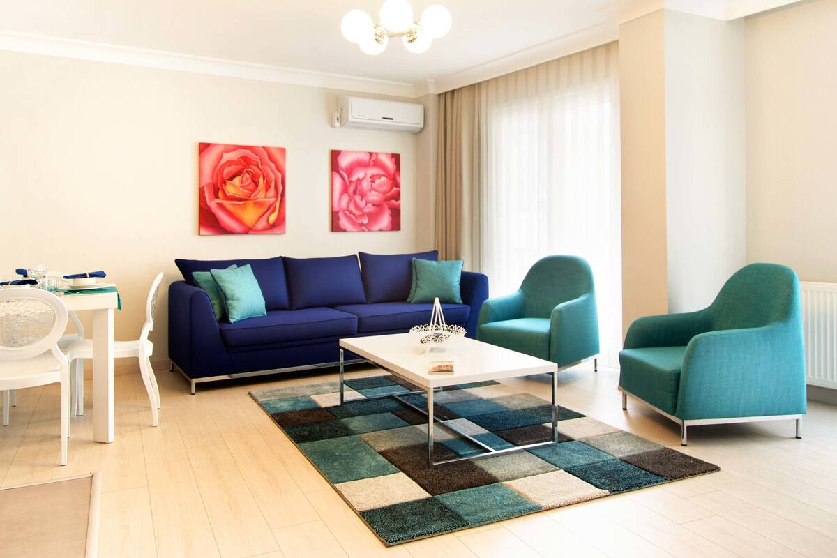 Un salon moderne avec un canapé bleu, des fauteuils turquoise, une table basse blanche et un tapis à motifs.