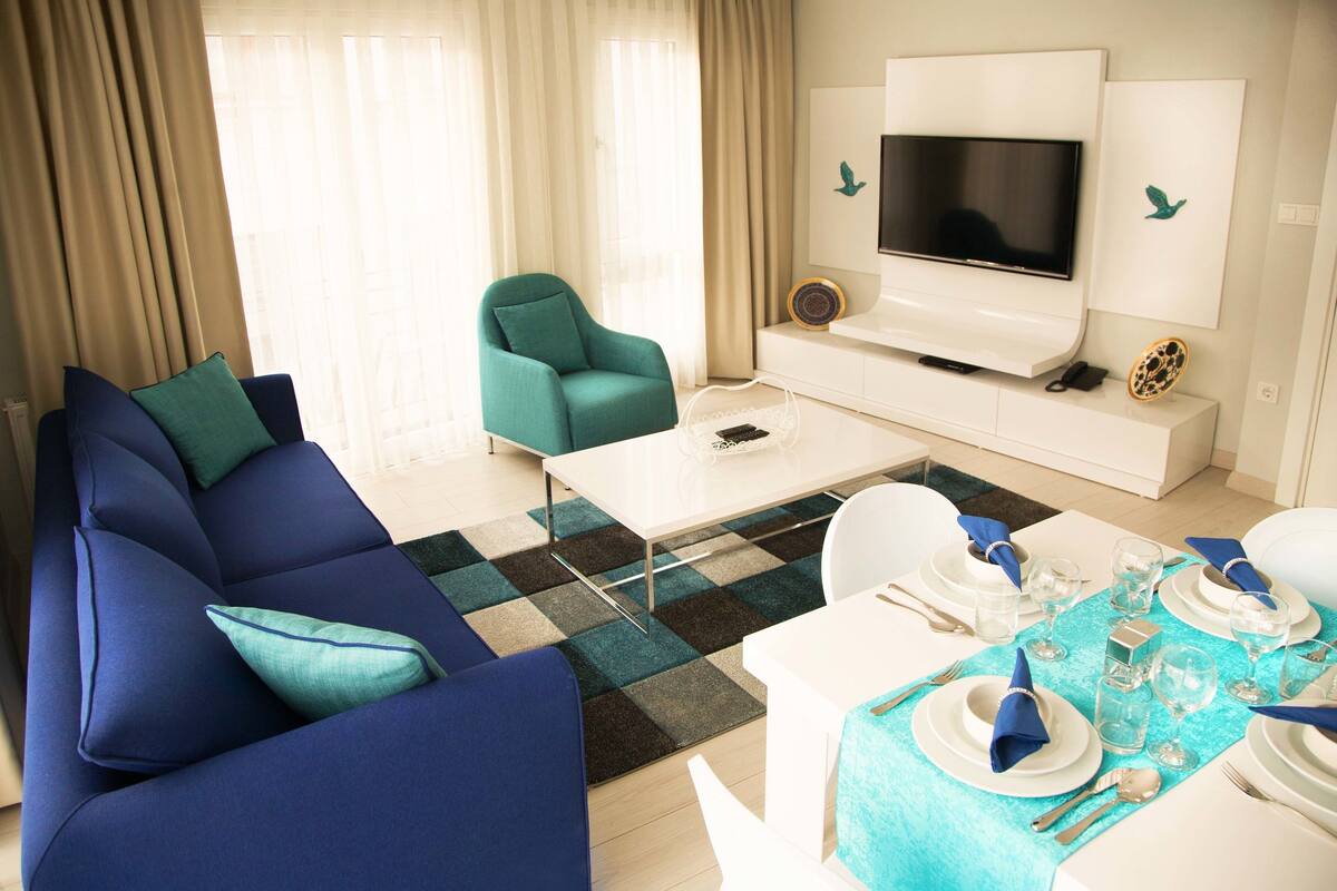Un salon moderne avec un canapé bleu, un fauteuil turquoise et un coin repas aménagé pour un repas.