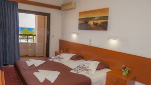 Habitación de hotel con una cama grande, una mesita de noche, una pequeña mesa con un jarrón y un cuadro en la pared.