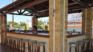 Un área de bar al aire libre con terraza de madera, pilares de piedra y taburetes de bar.