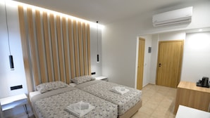 Una habitación de hotel moderna con dos camas, cabecero de madera, mesitas de noche, un escritorio y un equipo de aire acondicionado.