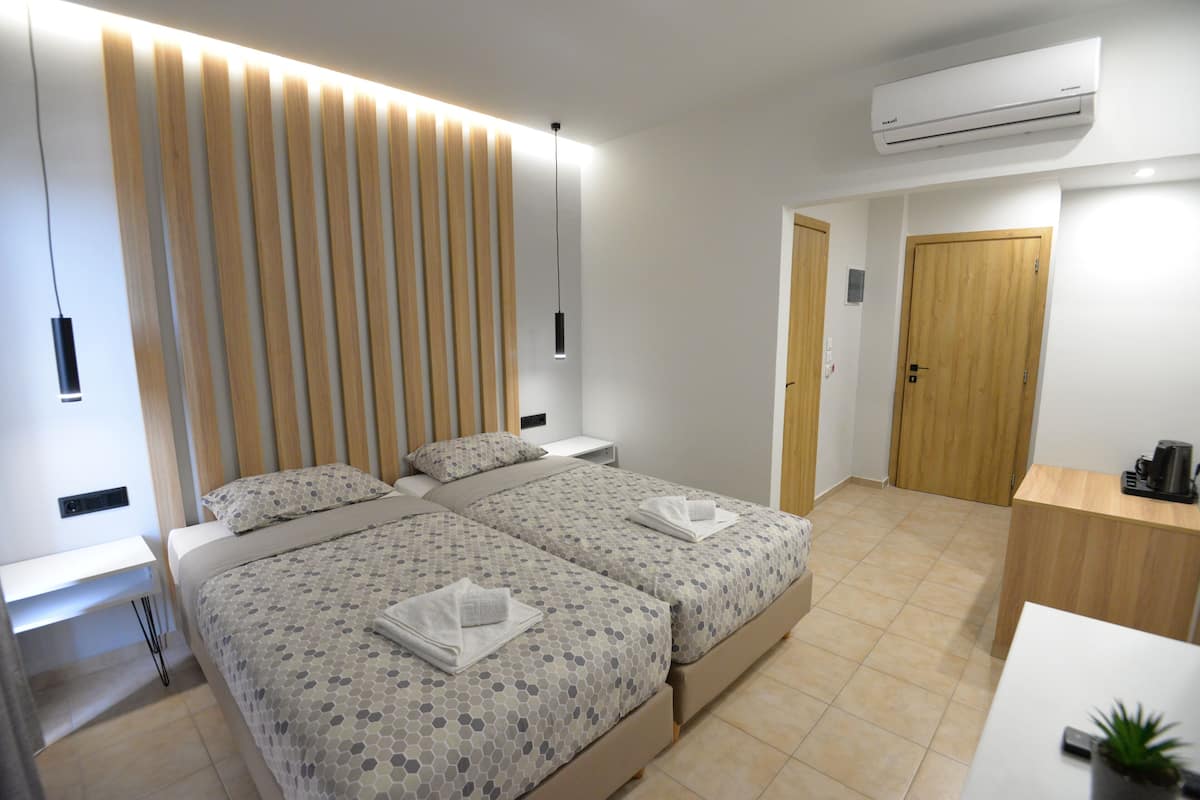 Ein modernes Hotelzimmer mit zwei Betten, einem Holzkopfteil, Nachttischen, einem Schreibtisch und einer Klimaanlage.