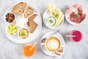 A breakfast setting with bread, yogurt, cheese, cured meats, and a coffee drink. - Mynext - Augarten Hostel (Vienna)