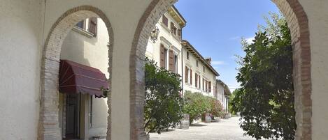 An outdoor courtyard with a covered seating area, brick arches, and a building with a red awning.