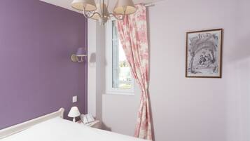 A bedroom with a bed, a nightstand, a lamp, a window with curtains, and a framed picture on the wall.