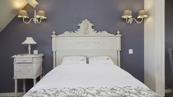 A bedroom with a white bed, two wall-mounted lamps, a nightstand with a lamp, and a decorative headboard.