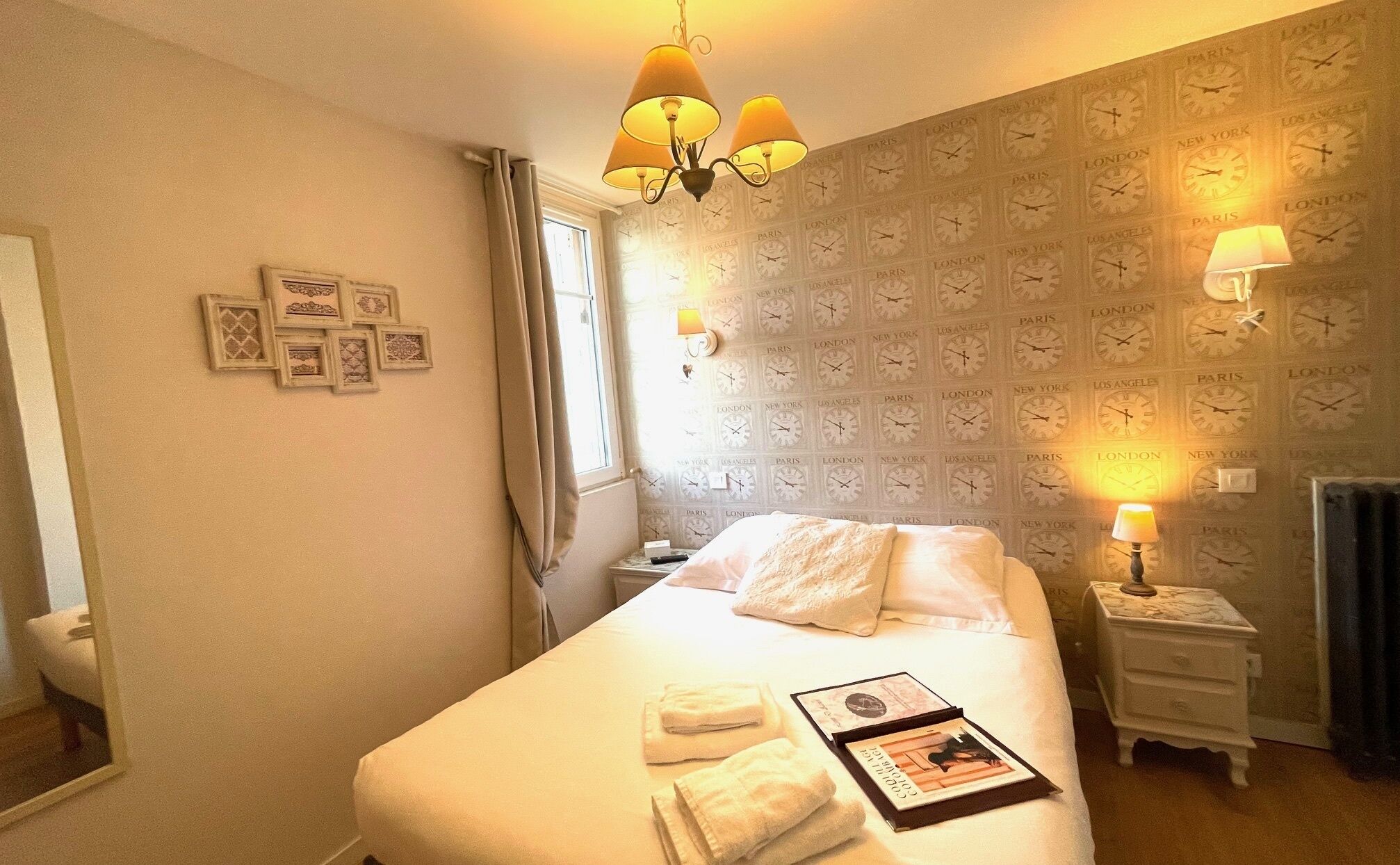 A hotel room with a bed, bedside lamps, a clock wallpaper, and a chandelier.