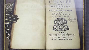 Un libro abierto titulado 'POESIES DE MALHERBE' con ornamentación metálica en la cubierta.