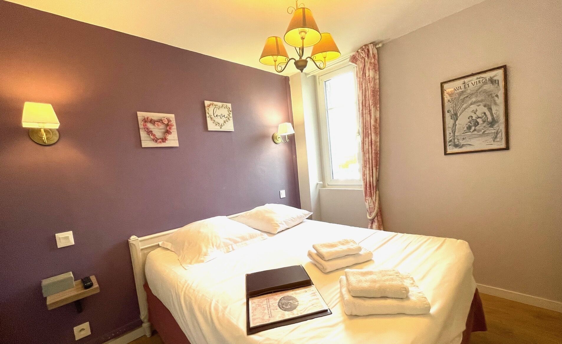 A hotel room with a bed, a bedside table, a lamp, and a window with curtains.