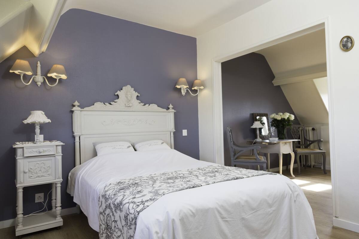 Un dormitorio con una cama blanca, una mesita de noche con lámpara y un escritorio con silla.