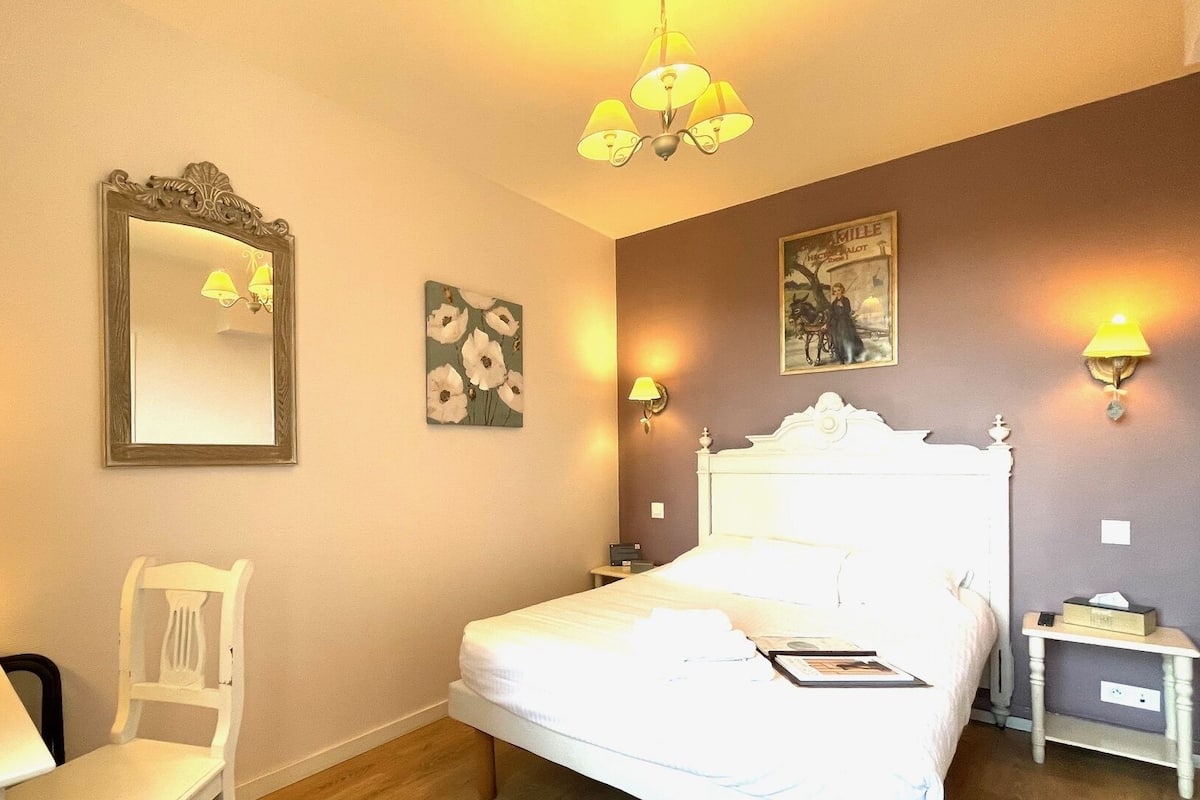 Una habitación de hotel con cama, una silla, un escritorio, una lámpara y luces en la pared.