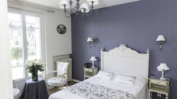 Un dormitorio con una cama grande, una silla, una mesa con un florero y vistas a un edificio.