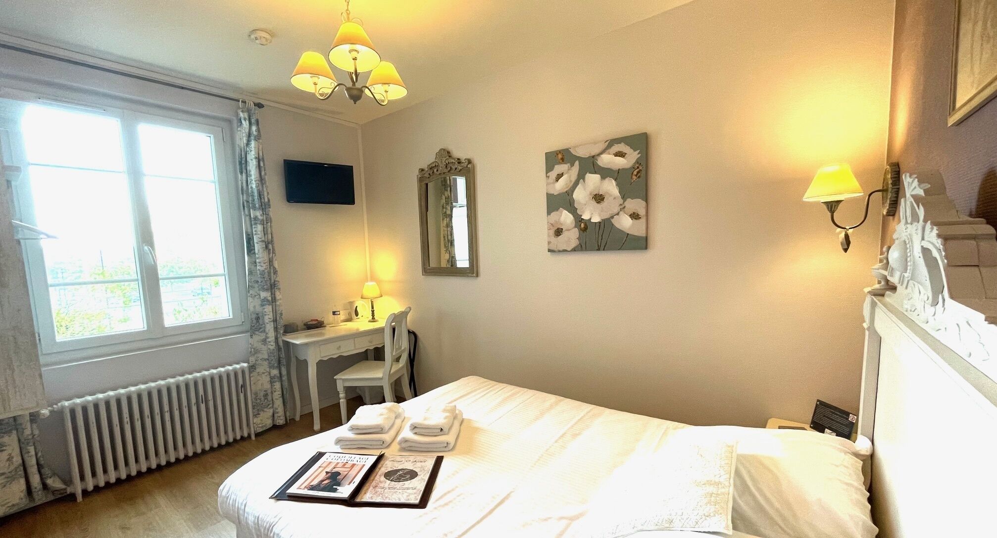 Een slaapkamer met een bed, een bureau, een stoel, een radiator, een raam en wandlampen.