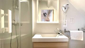 A modern bathroom with a glass shower enclosure, a white sink, and a hairdryer mounted on the wall.
