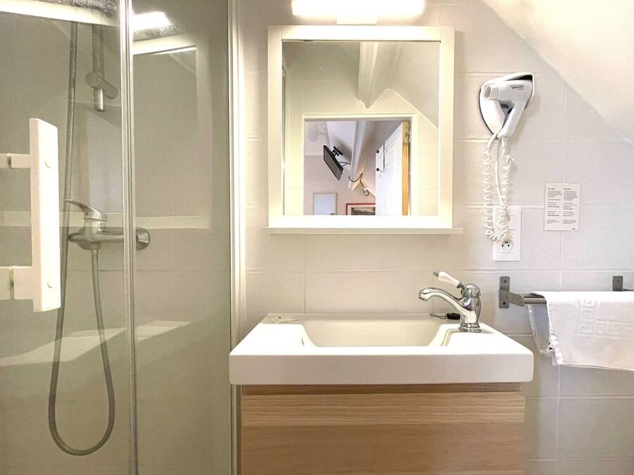 A modern bathroom with a glass shower enclosure, a white sink, and a hairdryer mounted on the wall.