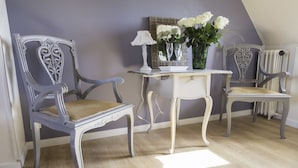 Una habitación con dos sillones de estilo antiguo, una mesita con una lámpara y un jarrón con flores.
