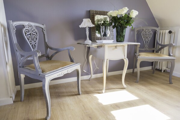 Una habitación con dos sillones de estilo antiguo, una mesita con una lámpara y un jarrón con flores.