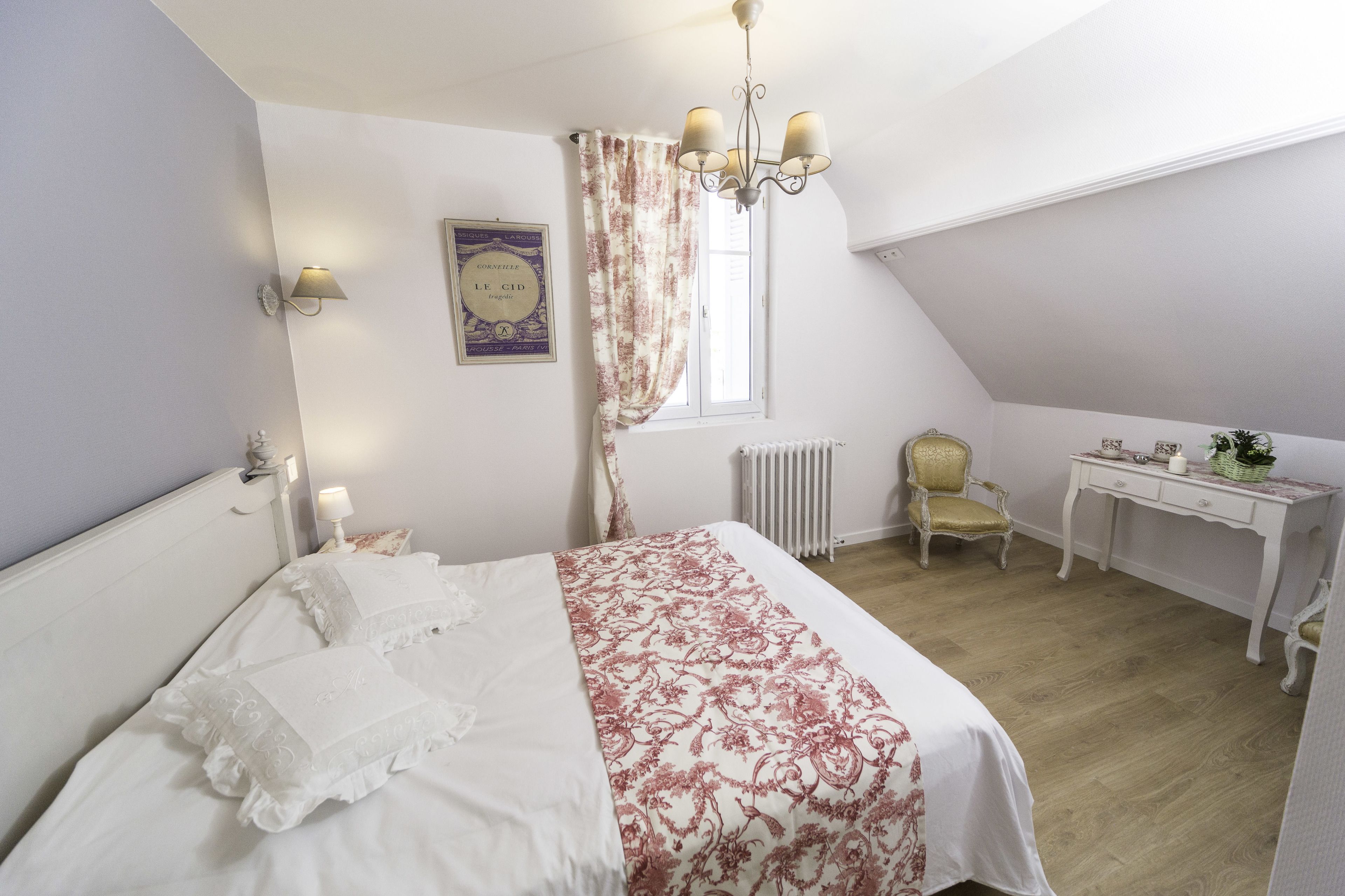 A bedroom with a bed, a chair, a desk, a radiator, and a chandelier.