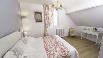 A bedroom with a bed, a chair, a desk, a radiator, and a chandelier.