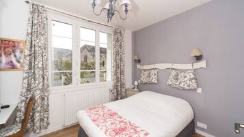A bedroom with a large bed, a window with curtains, a chandelier, and a wall-mounted lamp.