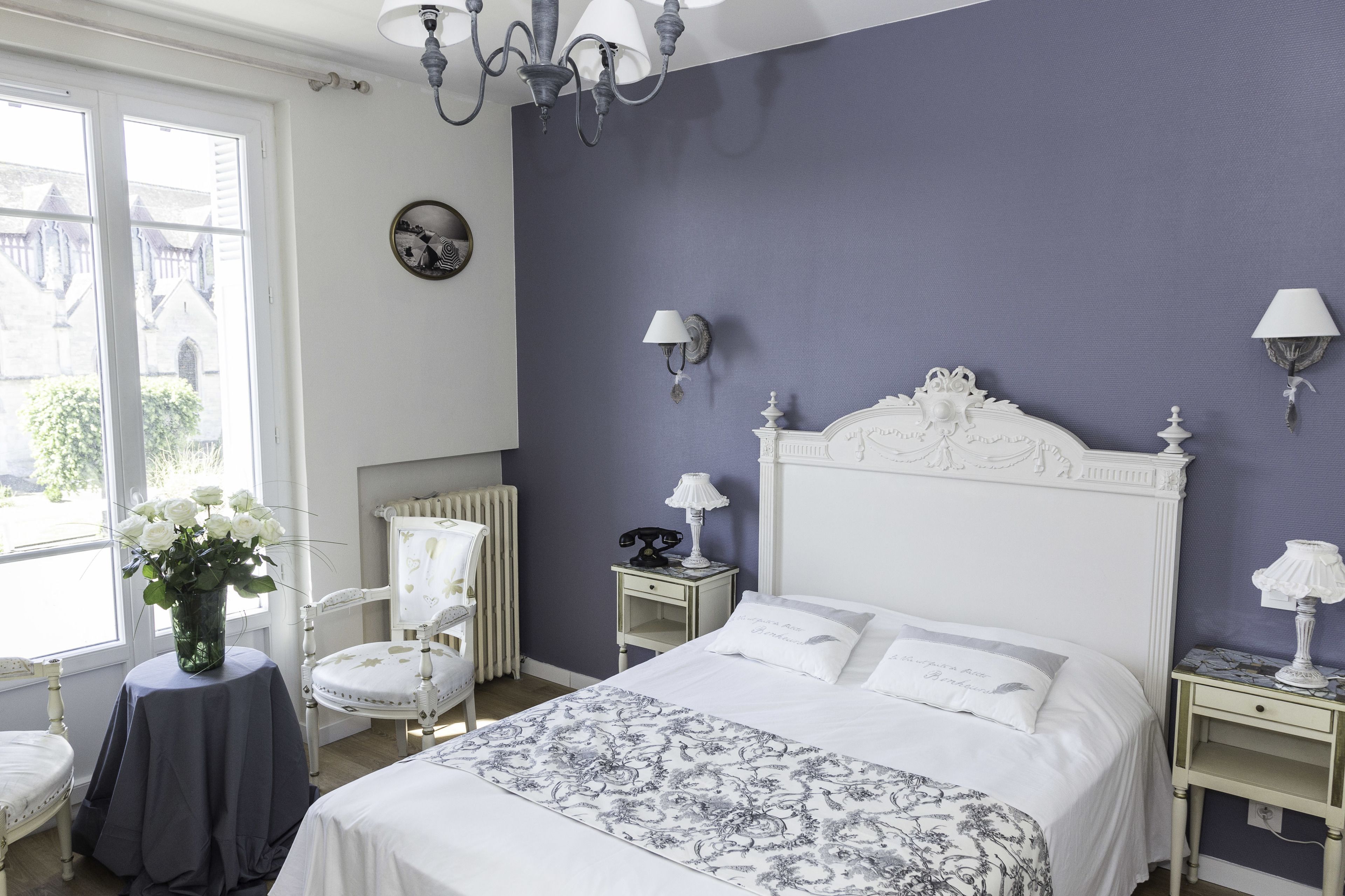 A bedroom with a white bed, a chair, a nightstand, and a lamp.