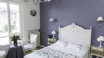 A bedroom with a white bed, a chair, a nightstand, and a lamp.