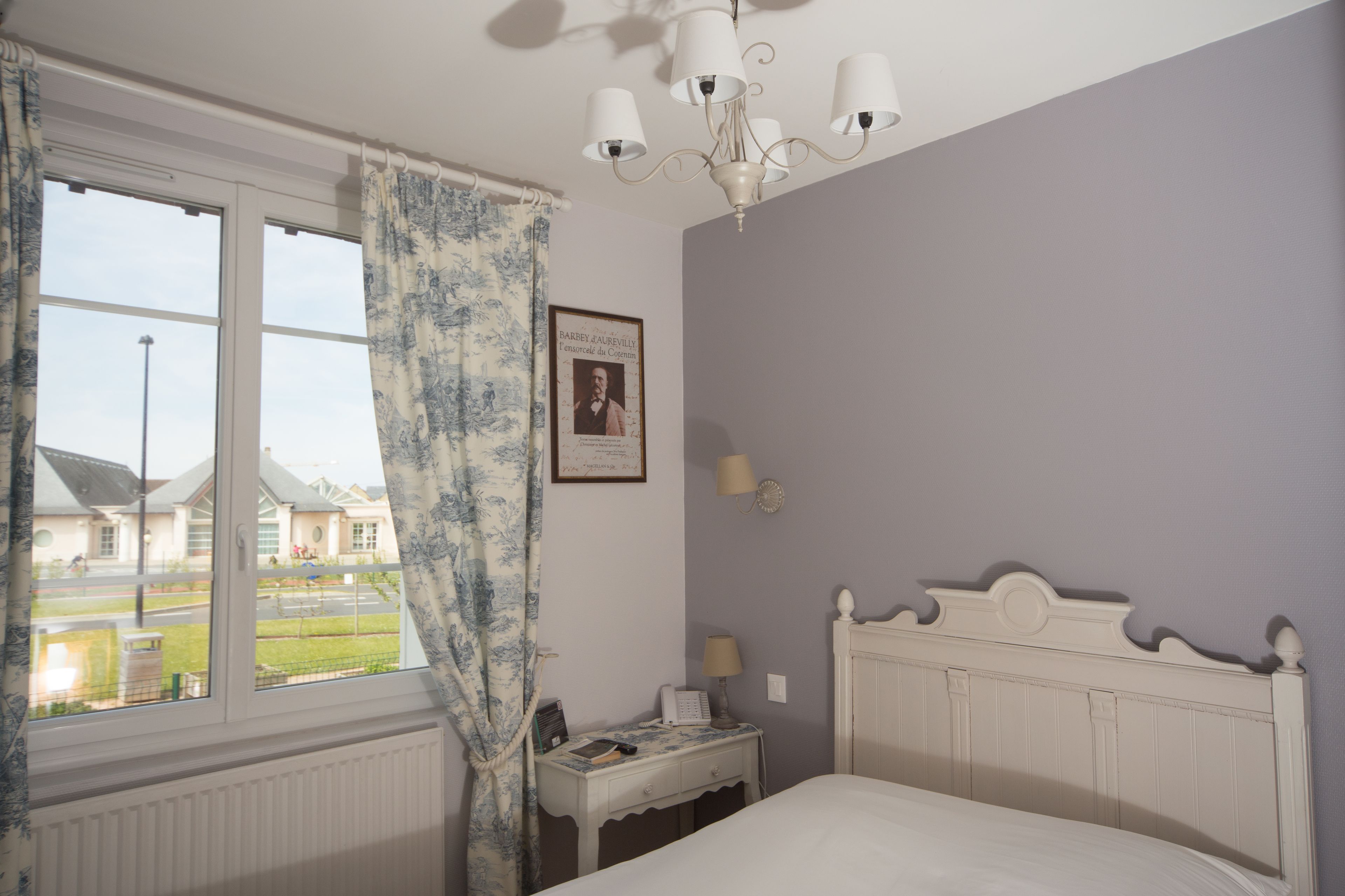 A bedroom with a bed, a bedside table, a lamp, a framed picture on the wall, and a window with curtains.