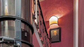A grand staircase with a glass elevator, ornate metal railings, and a wall-mounted light fixture. - Palazzo Branchi (Florence)