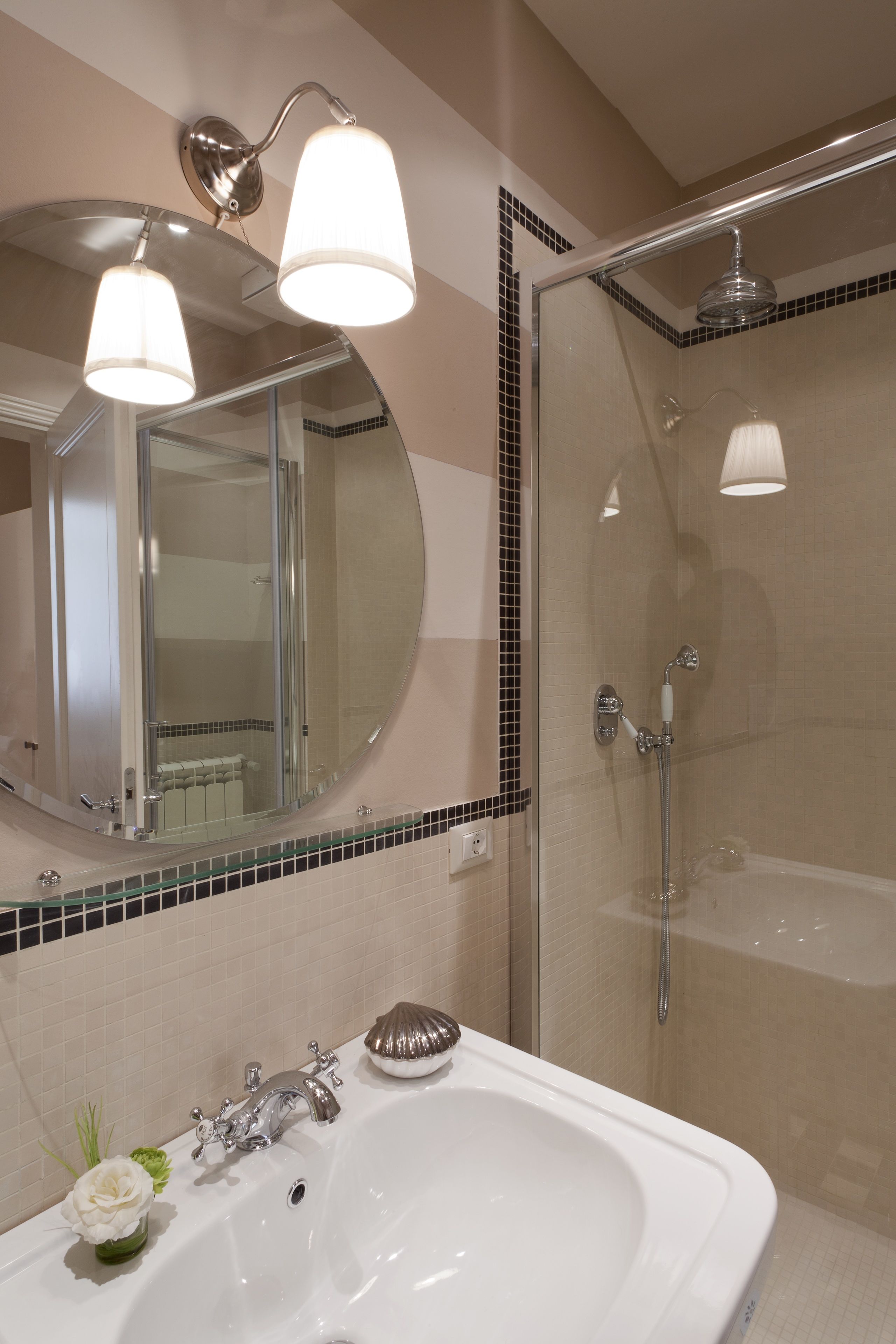 A bathroom with a large mirror, a sink, a glass-enclosed shower, and two wall-mounted lights.