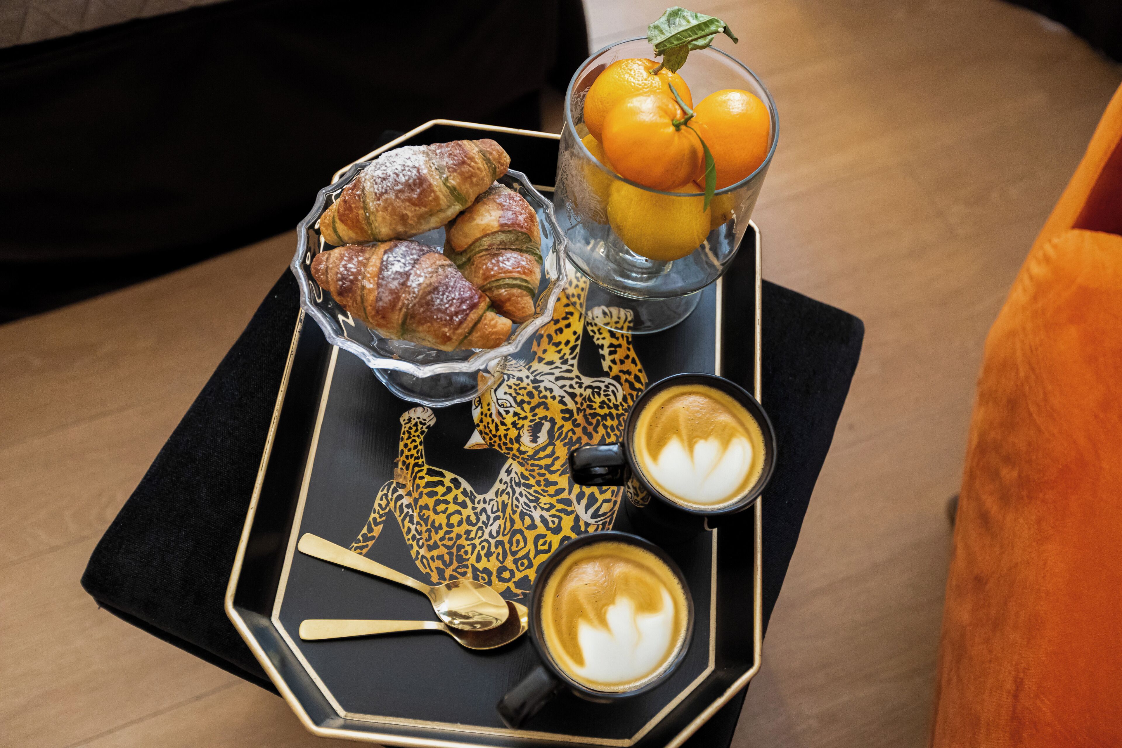 A tray with croissants, a glass of orange juice, a leopard-patterned teapot, and two cups of coffee.