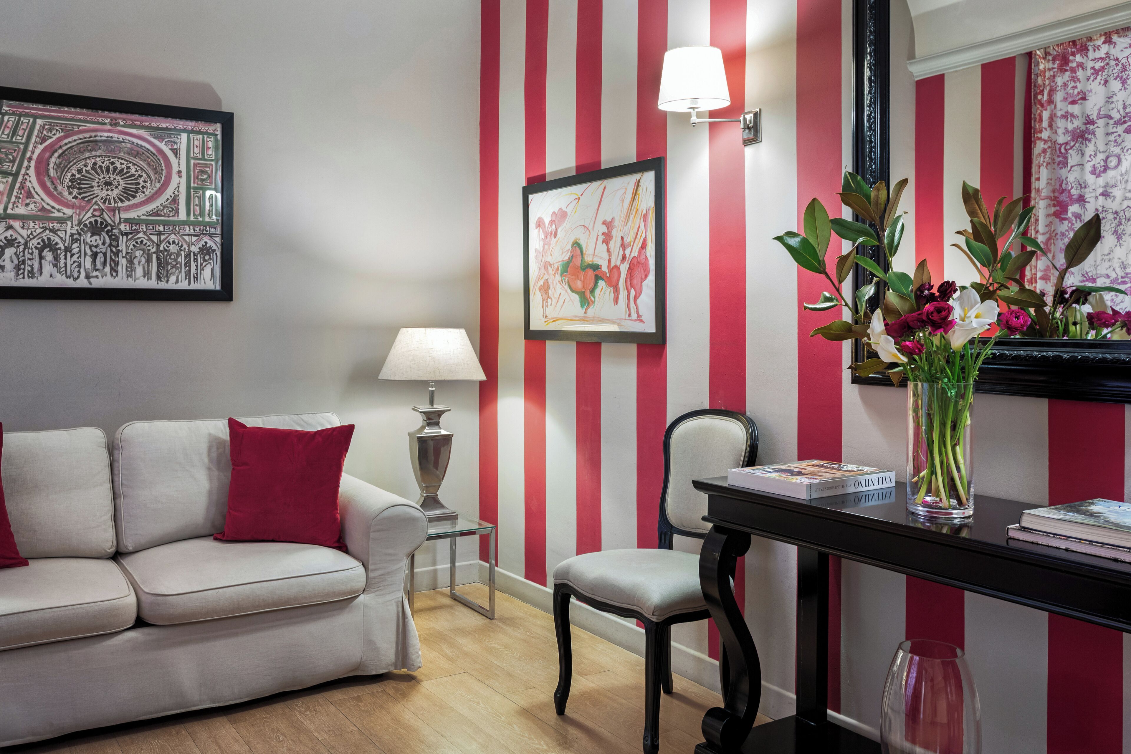 Una sala con pared a rayas, un sofá, una silla, una lámpara y un jarrón con flores.